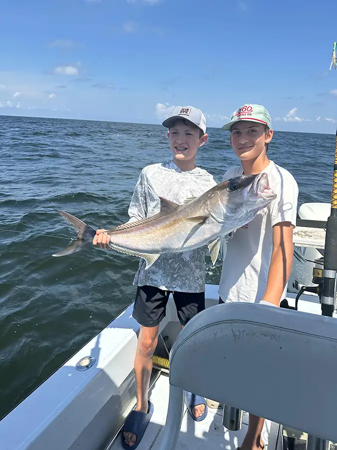 Two anglers holding a large amberjack on a charter boat in Gulf waters